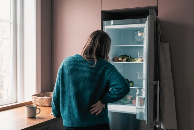 Frau steht vor einem geoeffneten Kuehlschrank und wirkt frustriert und ratlos.